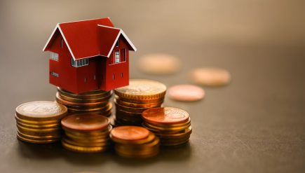 Miniaturowy dom na stosie monet. Pojęcie inwestycji w nieruchomości, pożyczek na nieruchomości, kredytów hipotecznych, podatków